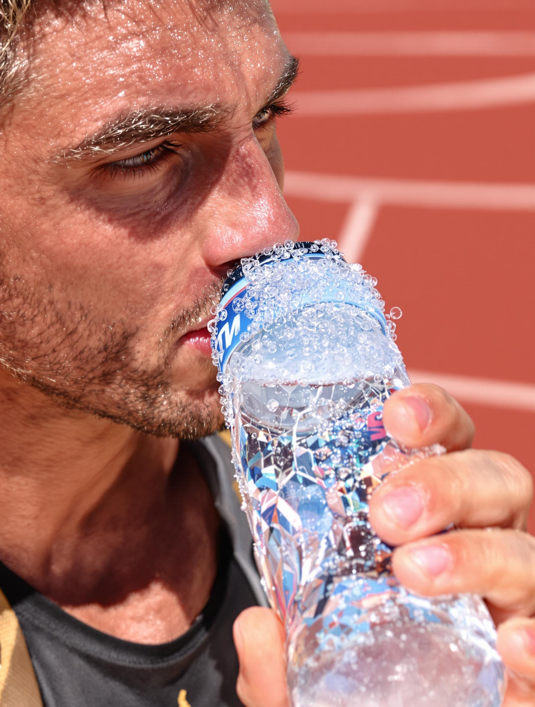 Un athlète buvant une gorgée d'eau gazeuse très fraîche dans un bidon sur une piste d'athlétisme